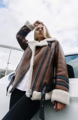 Kożuch damski w brązowym kolorze z białym futrem, z zamkiem błyskawicznym i skórzanymi paskami na rękawach