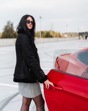 Czarny kożuch damski z kapturem, futrzanym wykończeniem i modnymi klamrami, idealny na zimowe dni